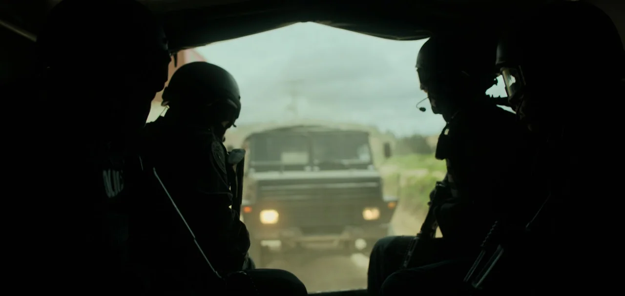 Triple Frontier (2019) movie still: medium — Four soldiers in tactical gear sit inside a dimly lit transport vehicle. A large military truck drives…