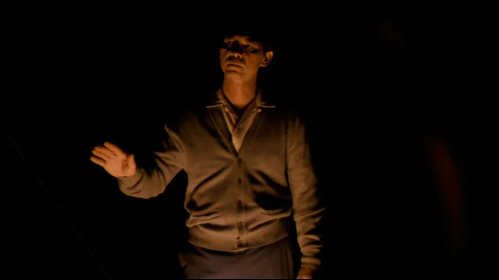 Che Part 2 (Guerrilla) (2008) movie still: medium — A man stands in a dark room with no visible walls or architectural features. He holds his right…