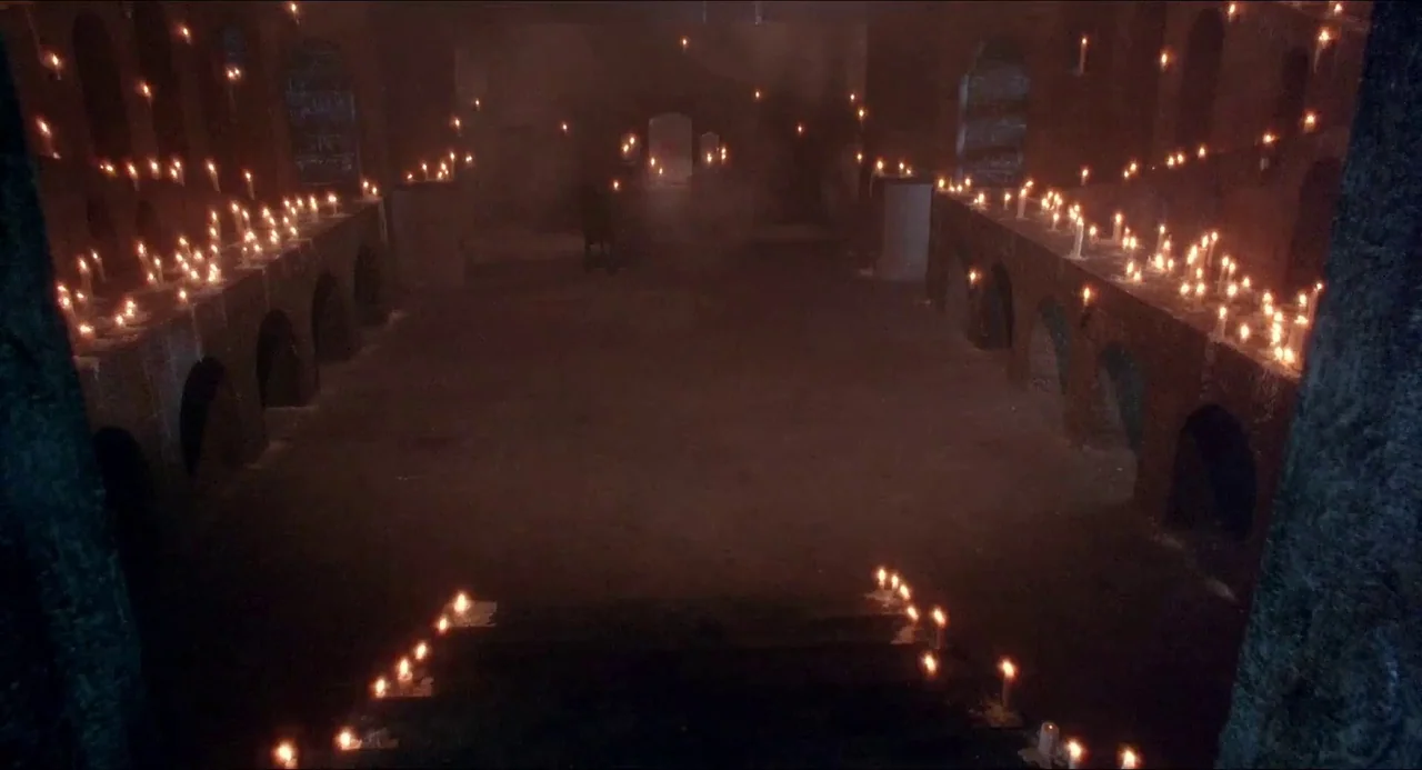 Hellbound: Hellraiser II (1988) movie still: wide — A large stone crypt with brick-arched recesses is filled with rows of lit candles. Small flames…