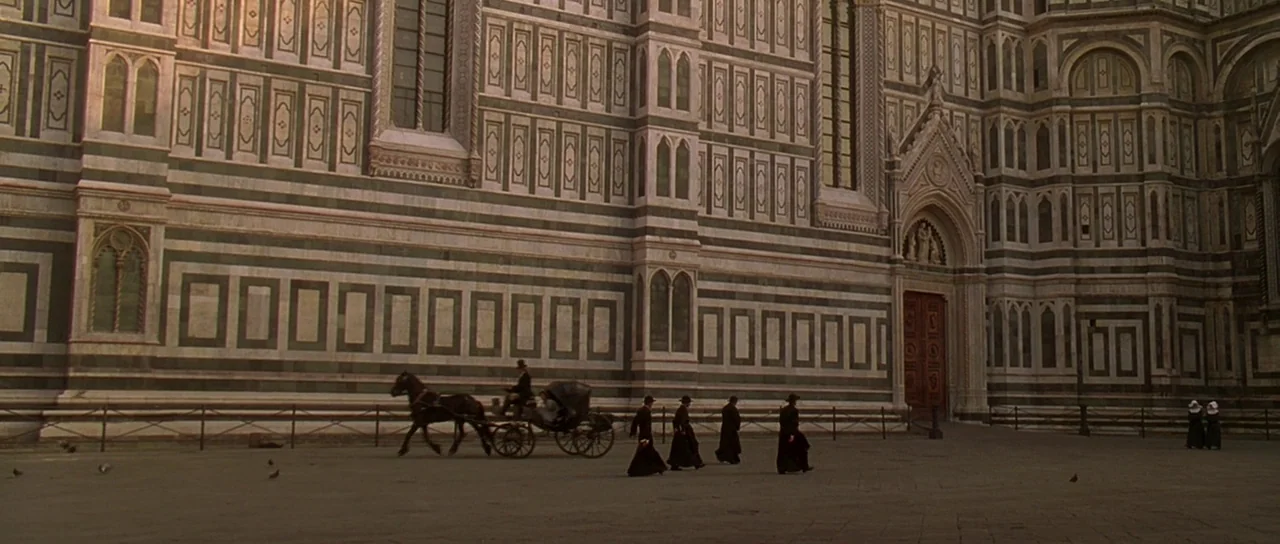 The Portait of a Lady (1996) movie still: wide — A massive white and green marble cathedral wall towers over an expansive stone plaza. Several men…