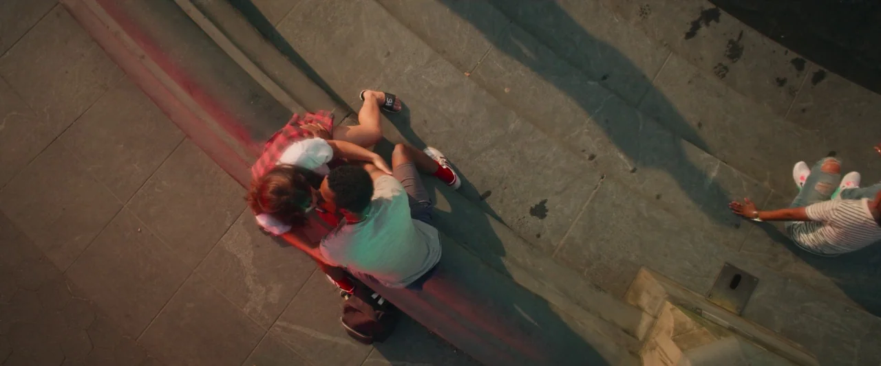 Someone Great (2019) movie still: wide — A set of broad stone steps sits in a public outdoor space at sunset. Three individuals occupy the steps,…