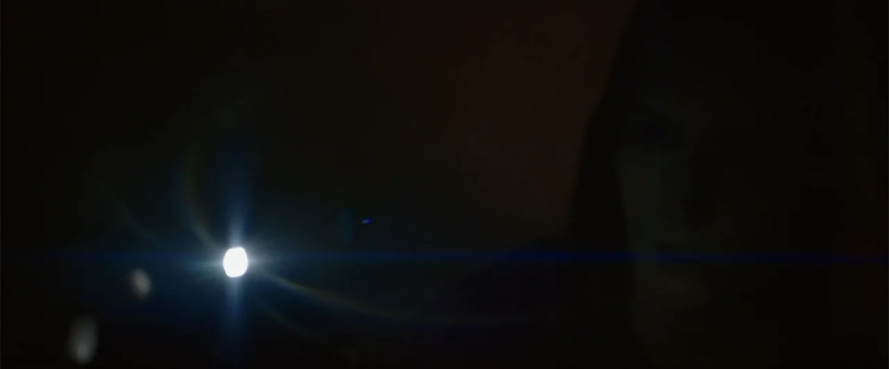 La herencia (2010) movie still: closeup — A dark, enclosed space is illuminated only by the concentrated beam of a flashlight. A person stands…