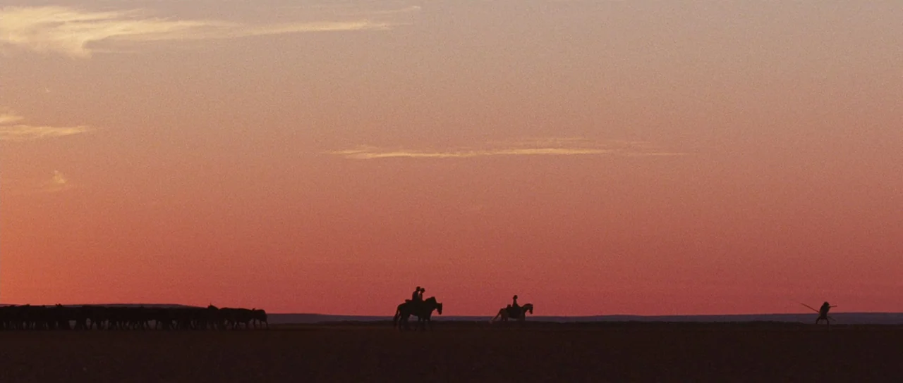Australia (2008) movie still: wide — A vast, flat prairie stretches toward the horizon under a soft pink sunset. Multiple riders on horseback and a…