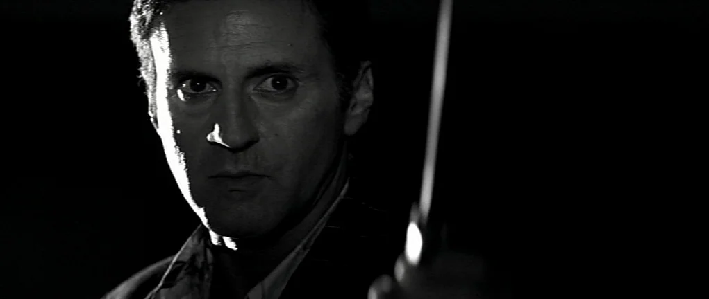 Girl on the Bridge (1999) movie still: closeup — A dark environment surrounds a man's face illuminated by a sharp side light. The man stares…