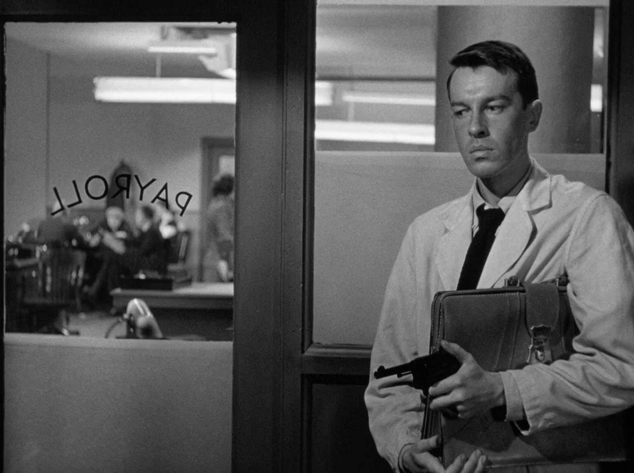 Gun Crazy (1950) movie still: medium — A man in a lab coat stands by a glass door marked with payroll lettering. Other people are working at desks…
