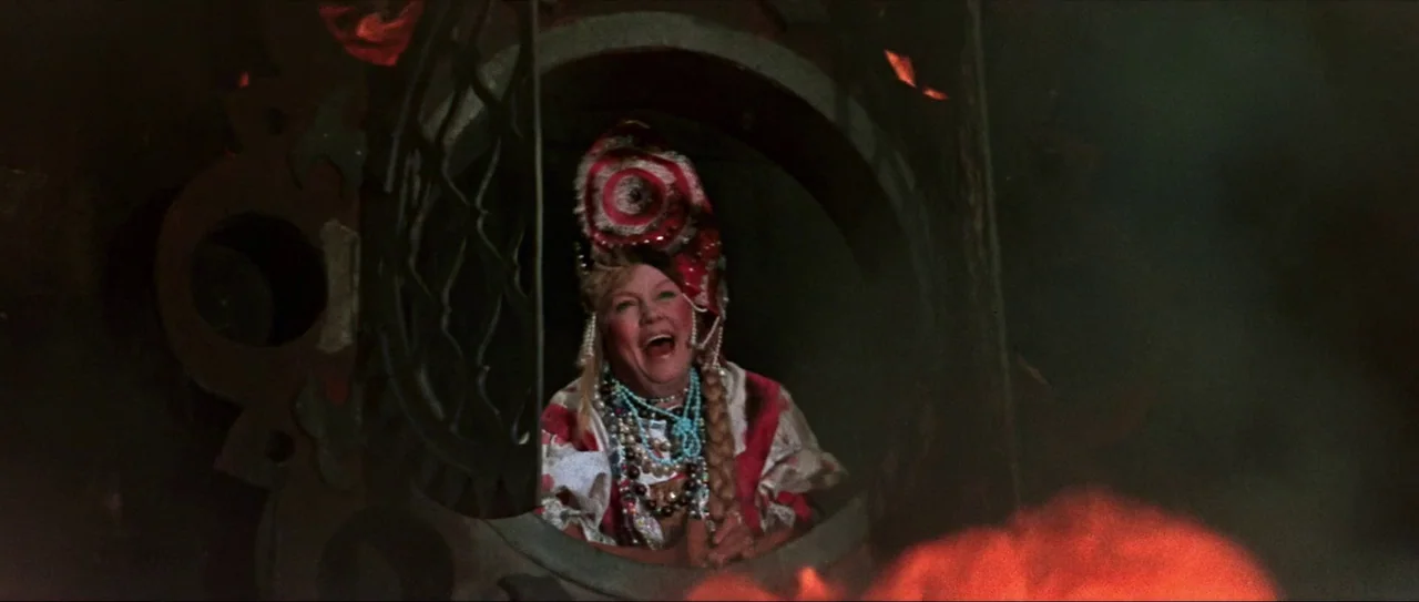 Through Fire, Water and… Brass Pipes (1968) movie still: medium — A woman looks out from a circular wooden opening in a dark environment. The scene…