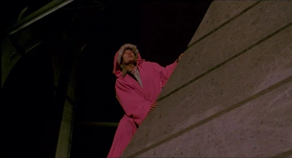 My Own Private Idaho (1991) movie still: medium — A man climbs the side of a concrete bridge pylon in the dark. He wears a bright pink hooded coat…