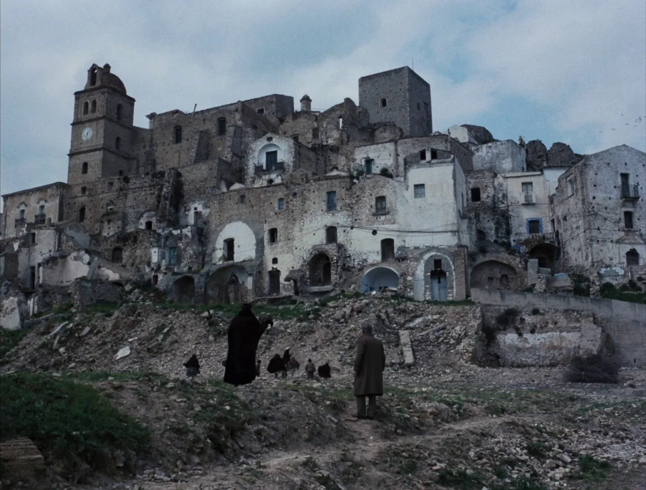 Christ Stopped at Eboli (1979) movie still: wide — A dense cluster of weathered stone buildings climbs a barren hillside under an overcast sky.…