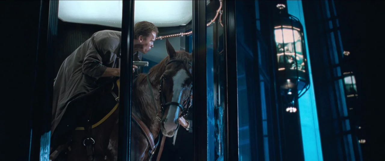 True Lies (1994) movie still: medium — A man in a trench coat rides a horse inside a modern glass elevator. Outside the elevator, the blue-lit…