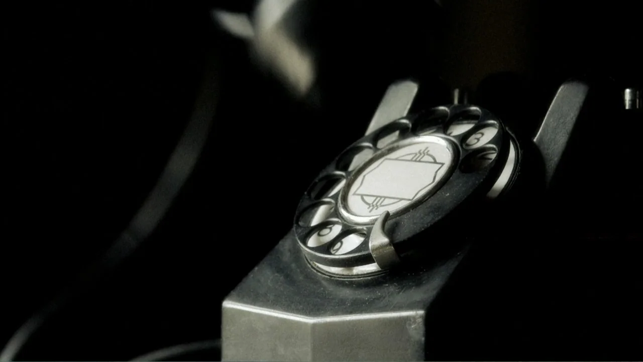 Alien Abduction: Betty and Barney Hill (2022) movie still: closeup — A close view of a dark rotary telephone dial sits in a dark room. The phone…