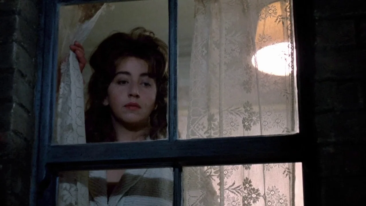 O Lucky Man! (1973) movie still: medium — A nighttime view through a wooden window frame with a textured white lace curtain. A woman stands behind…