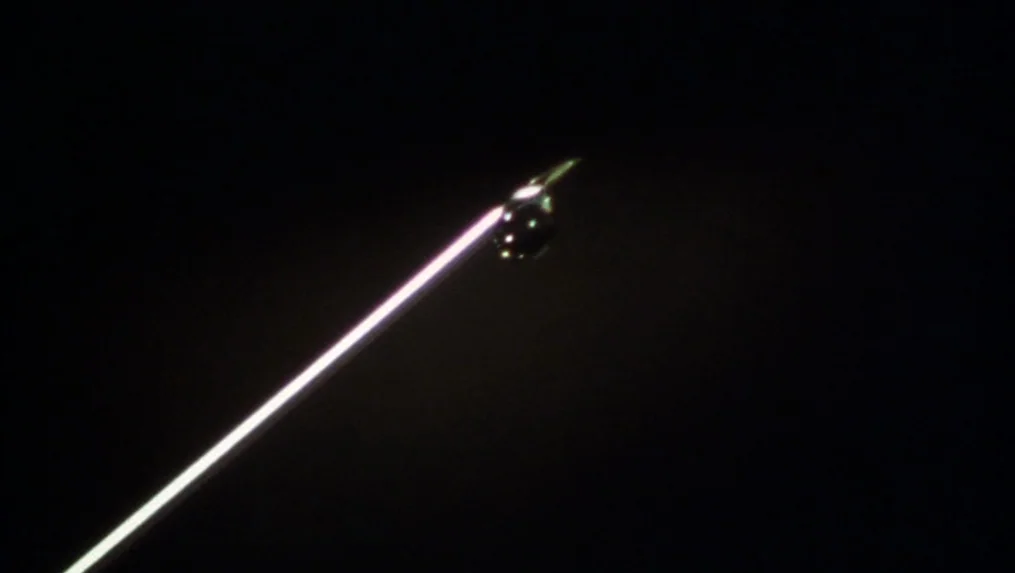 Martin (1977) movie still: closeup — A dark, featureless void contains a single sharp metallic point angled across the frame. A single spherical…
