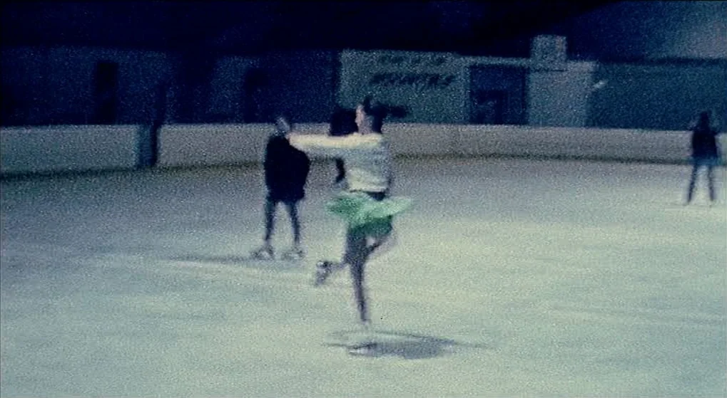 Julien Donkey Boy (1999) movie still: fullbody — An indoor ice rink with low-resolution grain and muted, cold lighting. A figure skater in a green…