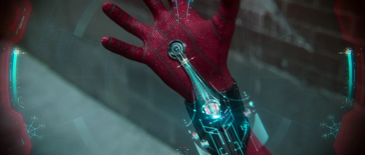 Spider Man: Homecoming (2017) movie still: closeup — A gloved red textured hand extends outward against a blurry urban brick wall background. A…