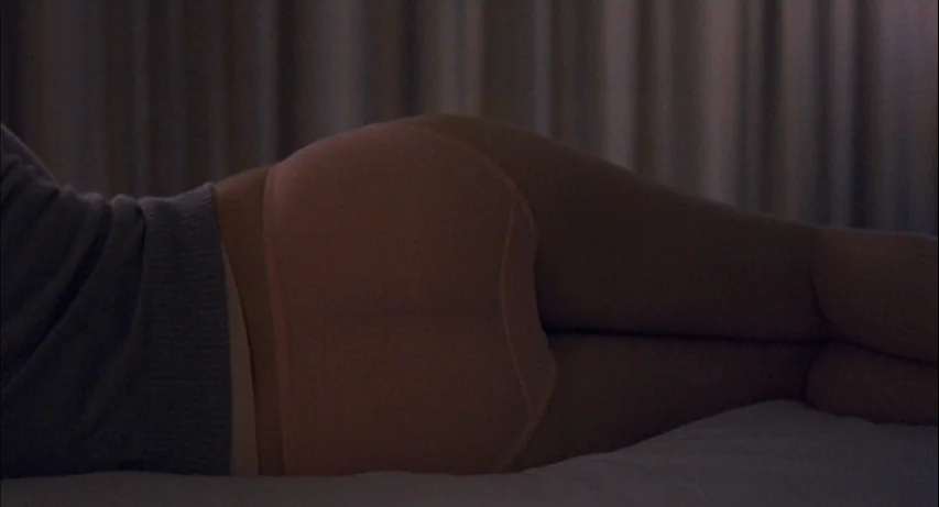 Lost In Translation (2003) movie still: closeup — A dark bedroom interior with vertical pleated curtains in the background. A woman lies on her side…