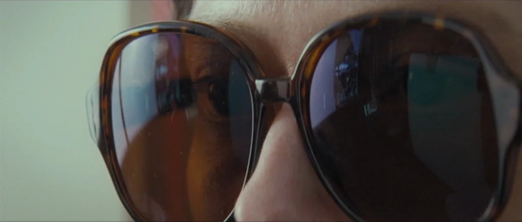 We Need To Talk About Kevin (2011) movie still: closeup — A close-up shot focuses on the lenses of large tortoiseshell-framed sunglasses. The lenses…