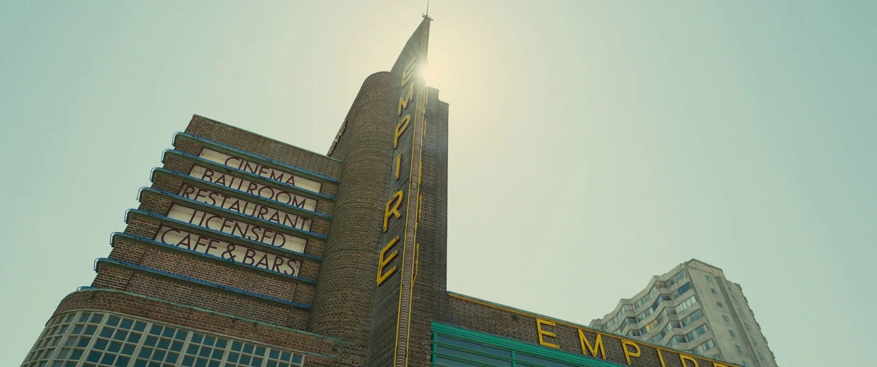 Empire of Light (2022) movie still: establishing — An Art Deco style brick building features multiple signage panels and a tall corner tower. The…