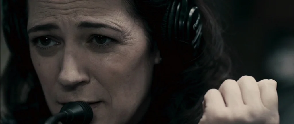 Pontypool (2008) movie still: closeup — A dimly lit professional audio recording environment with minimal equipment visible. A woman wearing black…