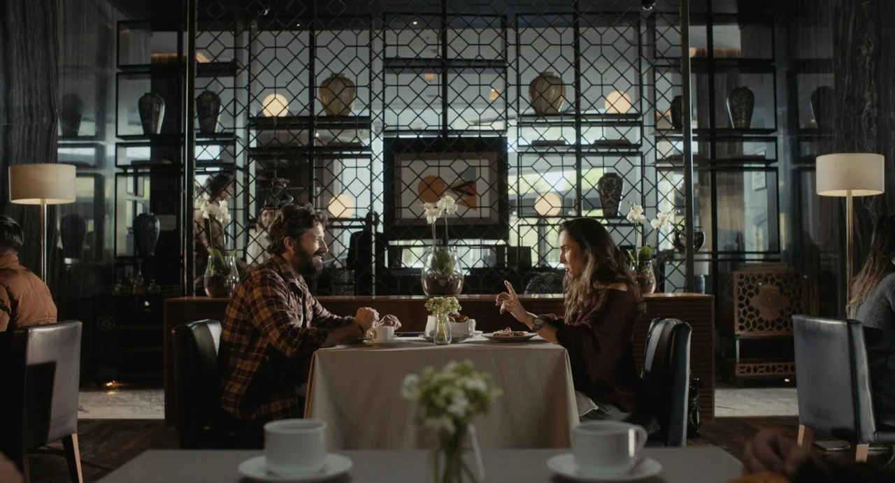 Dating Santa (2023) movie still: medium — A restaurant dining area features decorative metal screens and tables with white tablecloths. A man and a…