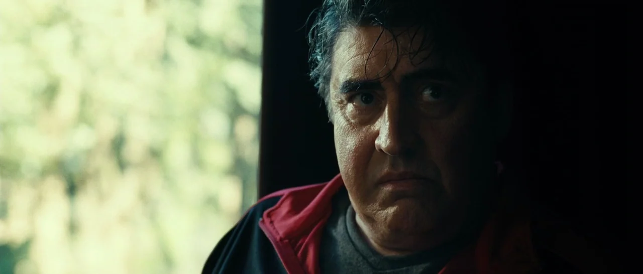 Message From The King (2016) movie still: closeup — A man sits inside a dim vehicle with blurred green foliage visible through the window. The…