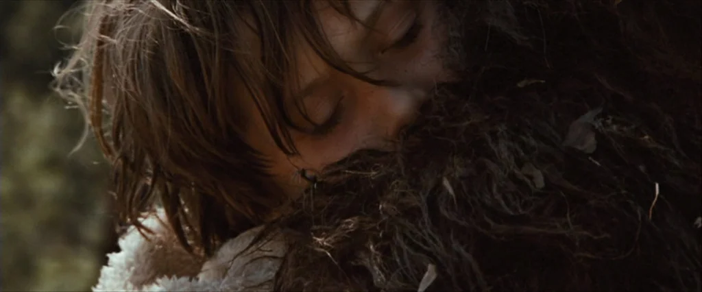 Where The Wild Things Are (2009) movie still: closeup — A close view of a child hugging a large, dark brown, shaggy creature outside. The child…