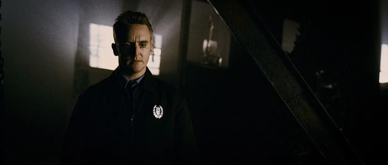 The Midnight Meat Train (2008) movie still: medium — A dimly lit industrial space features a dark steel beam and a bright window. A man in a dark…