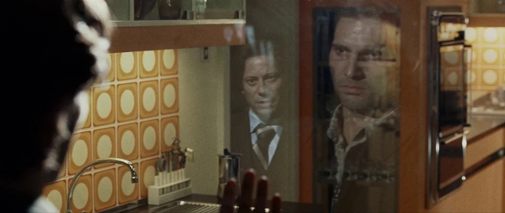 Munich (2005) movie still: medium — A 1970s kitchen features distinct orange and white geometric tiled walls. A man stares at the reflection of…