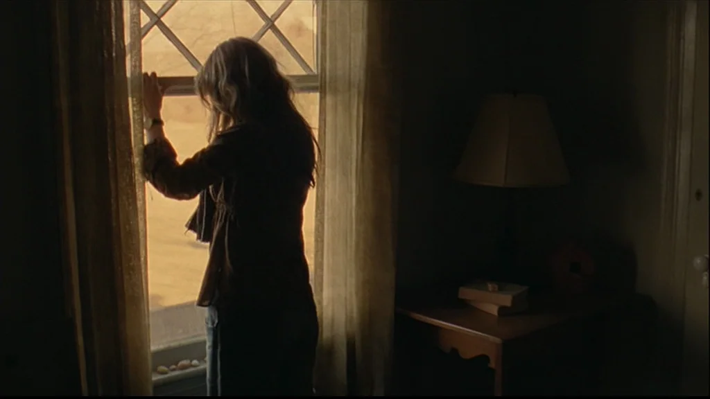 Margot At The Wedding (2007) movie still: medium — A dimly lit room features a wooden side table with books and a lamp. A woman in a dark shirt…