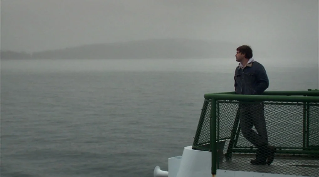 Your Sister’s Sister (2011) movie still: wide — A man stands on the deck of a boat surrounded by thick grey fog. The man rests his arms on a green…