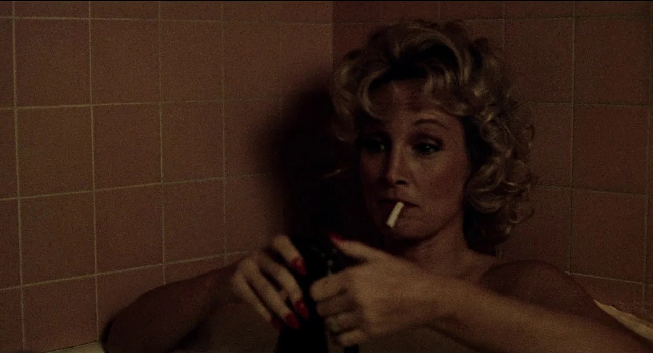 Desert Hearts (1985) movie still: medium — A woman sits in a tiled bathtub lined with rectangular pink tiles. She holds a small dark object in her…