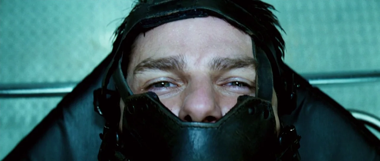Down With Love (2003) movie still: closeup — A man lies on a surface in an industrial room with teal tiled walls. He wears a tight leather mask…