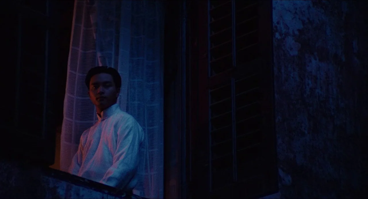 Rouge (1987) movie still: medium — A man stands framed by a darkened window in a cool blue night. Beside him, dark wooden shutters and a textured…