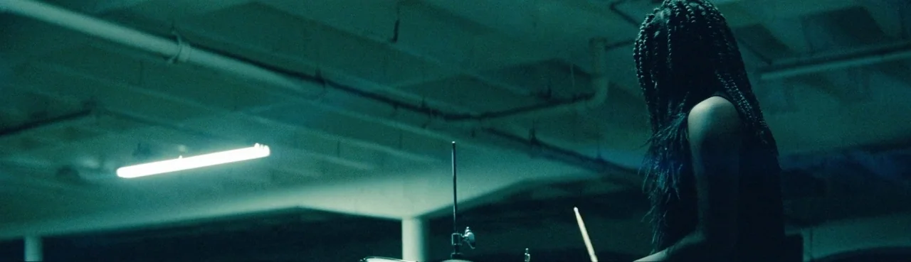 Lemonade (2016) movie still: medium — A dark, industrial-style space features high ceilings with exposed pipes and structural supports. A woman with…