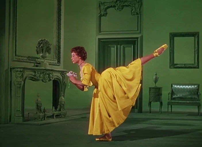 An American In Paris (1951) movie still: fullbody — A green-walled room features ornate moldings, a fireplace, and classic furniture pieces. A young…
