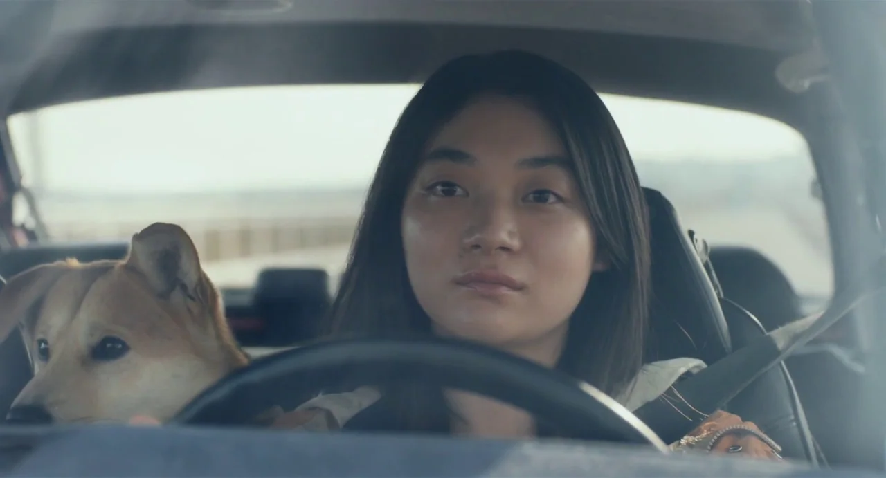 Drive My Car (2021) movie still: medium — The interior of a car during the daytime with a blurry road visible outside. A young woman drives the…