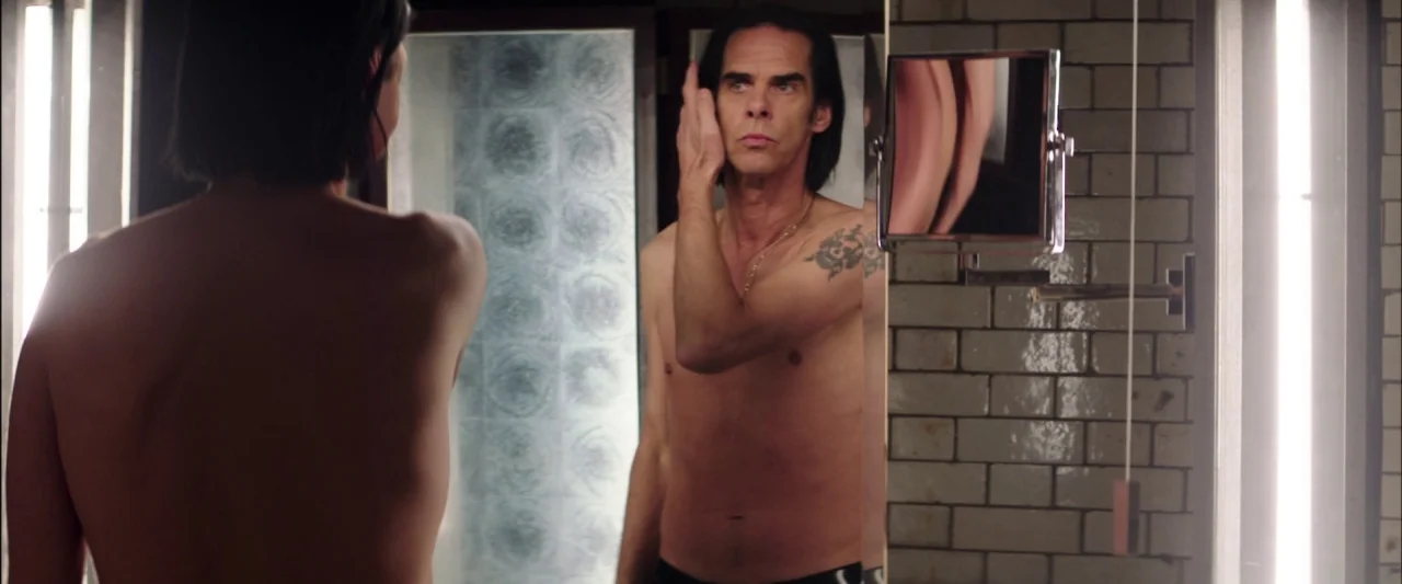 20,000 Days on Earth (2014) movie still: medium — A tiled bathroom features vertical fluorescent lights positioned on both sides of a mirror. A slim…