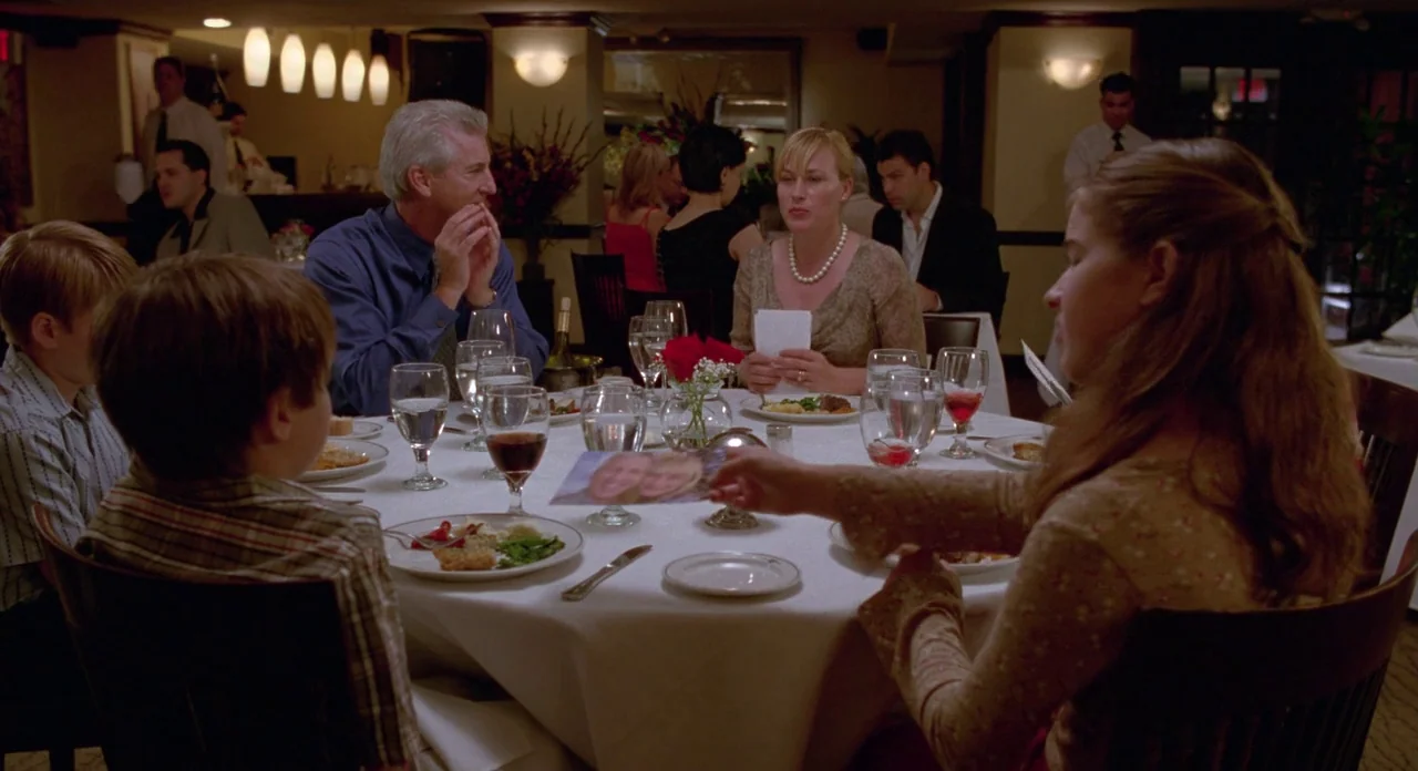Boyhood (2014) movie still: medium — A group of people sit around a circular white-clothed table in a dimly lit restaurant. A young woman passes a…