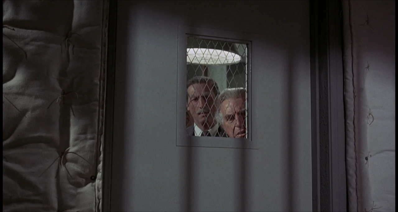 The Dunwich Horror (1970) movie still: medium — A padded door features a rectangular wired glass observation window with a metal frame. Two men look…