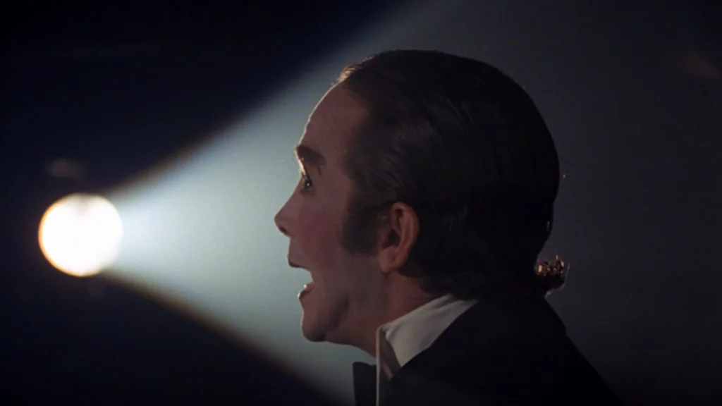 Cabaret (1972) movie still: closeup — A dark, empty space is illuminated by a single concentrated beam of light. A man in a tuxedo stands in…