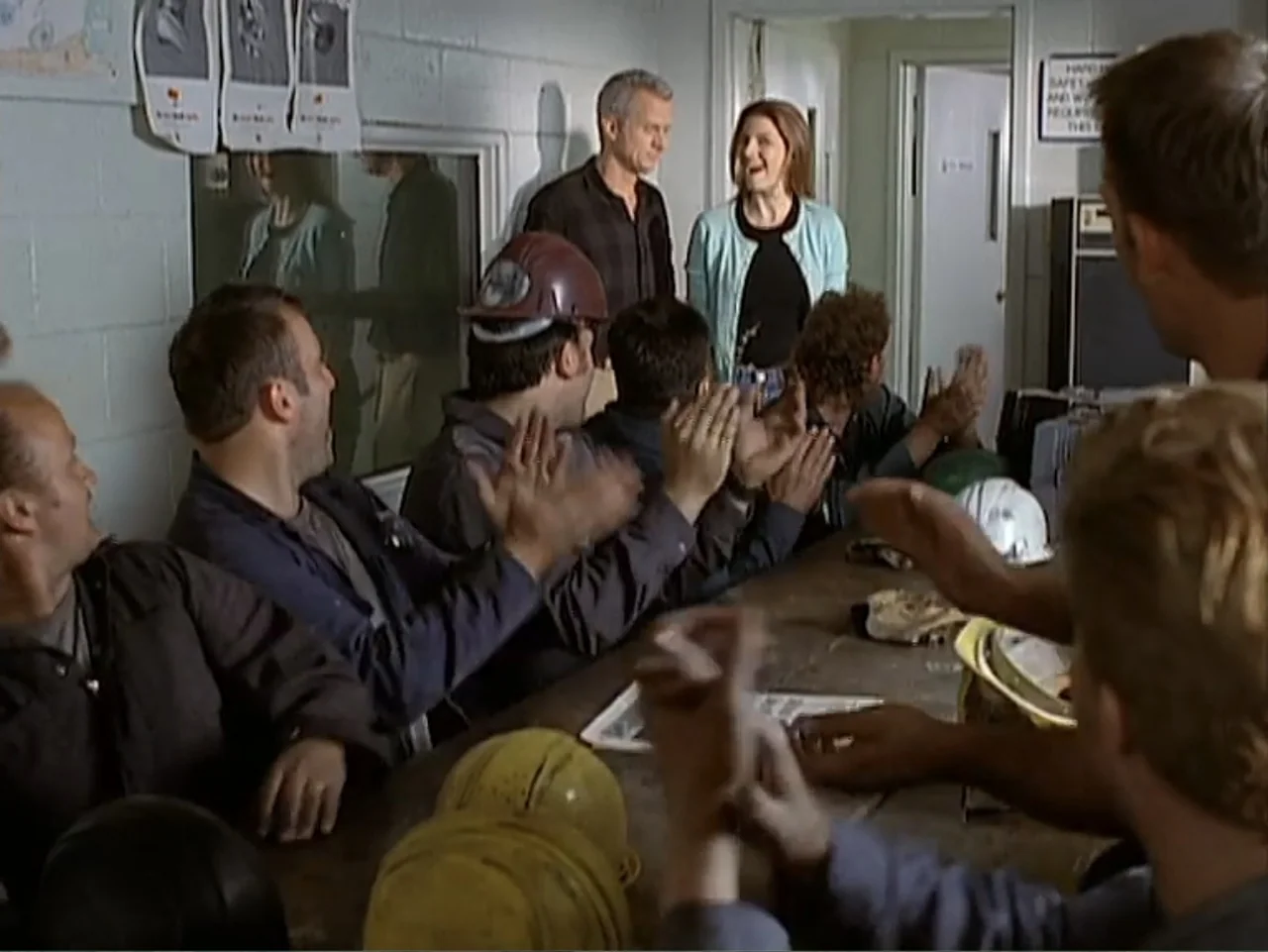 Catch a Falling Star (2000) movie still: medium — A utilitarian break room with concrete block walls and a long wooden table. Several men in work…