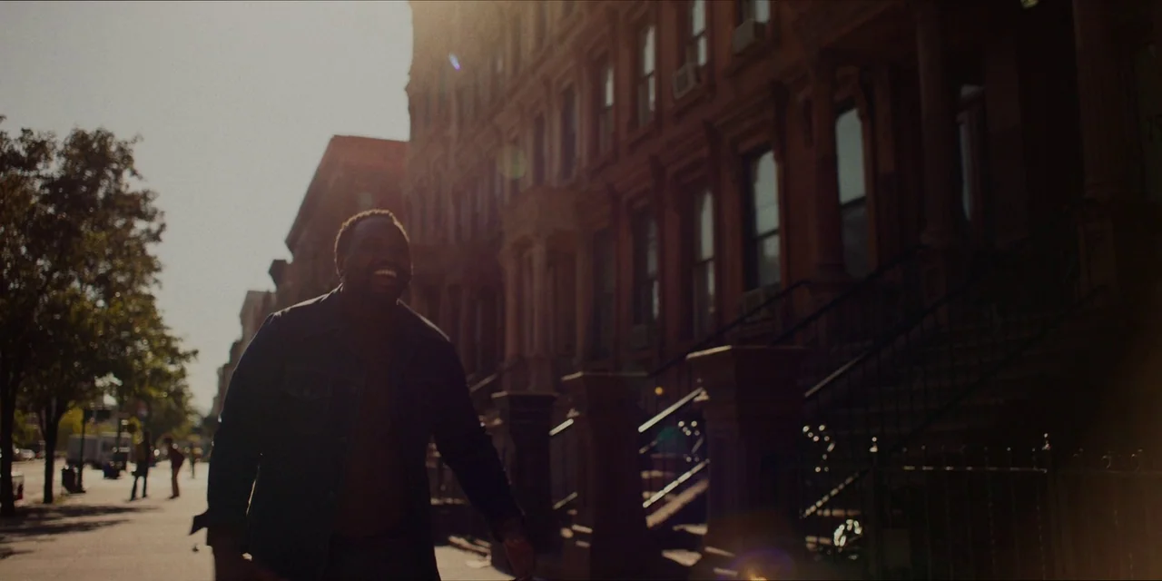 If Beale Street Could Talk (2018) movie still: medium — A sidewalk runs alongside a row of classic New York city brownstone buildings. A man in a…