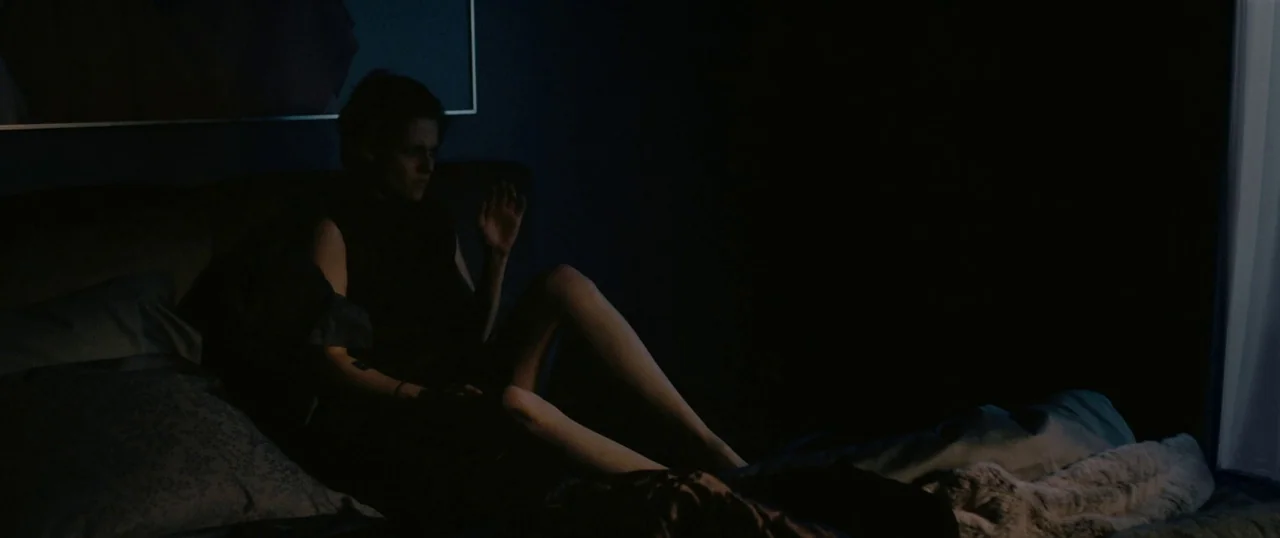 Personal Shopper (2016) movie still: medium — A dimly lit room at night features a person sitting on an unmade bed. The subject sits among pillows…