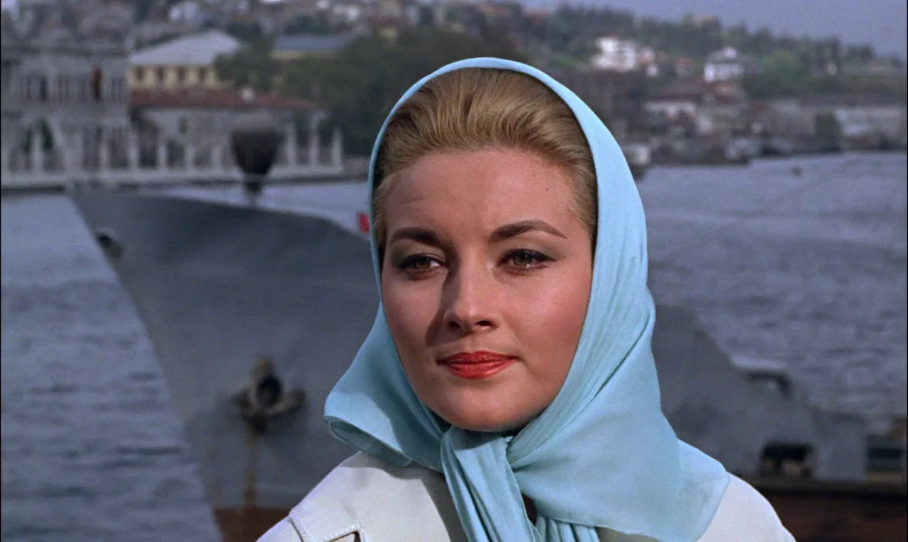 From Russia With Love (1963) movie still: closeup — A woman stands in the foreground near a harbor with a large vessel behind. She looks toward the…