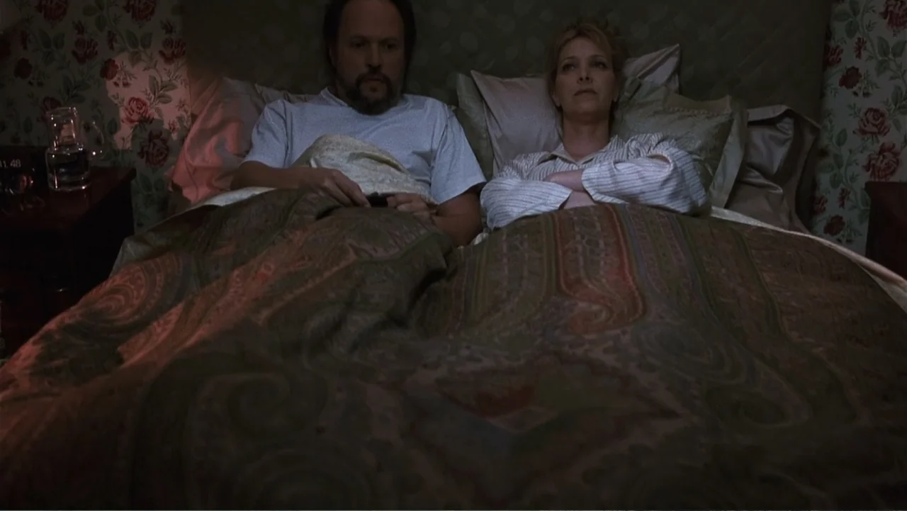 Analyze That (2002) movie still: medium — A dark bedroom features floral wallpaper and a bed with a patterned comforter. A man and a woman lie side…