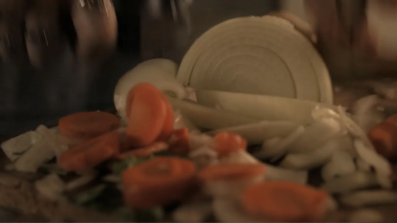 A Boyfriend for My Wife (2008) movie still: closeup — A close-up view shows sliced carrots and onions on a wooden cutting board. Hands are visible…