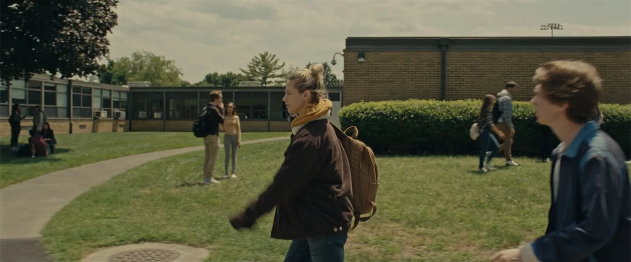 Chemical Hearts (2020) movie still: medium — A school courtyard with brick buildings and grassy lawns under a bright sky. A young woman walks across…