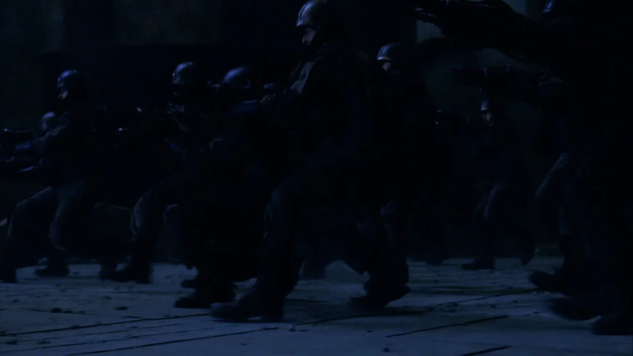 The Chronicles of Riddick (2004) movie still: medium — A group of tactical soldiers maneuvers across a dark, paved exterior at night. The…