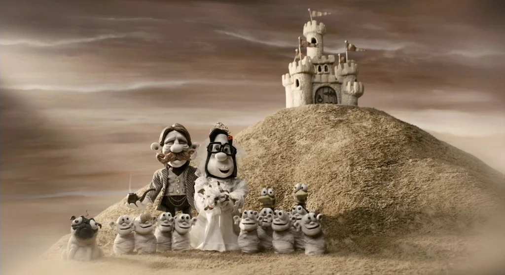 Mary & Max (2009) movie still: wide — A miniature sandy hill with a toy castle sits under a vast brown sky. A group of clay figures stands in the…