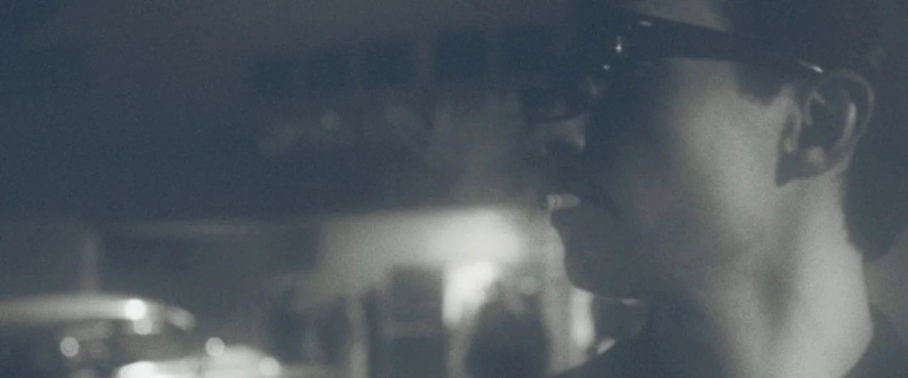 The Vast of Night (2019) movie still: closeup — A dark, blurred parking lot environment at night with soft ambient glows in distance. A young man in…