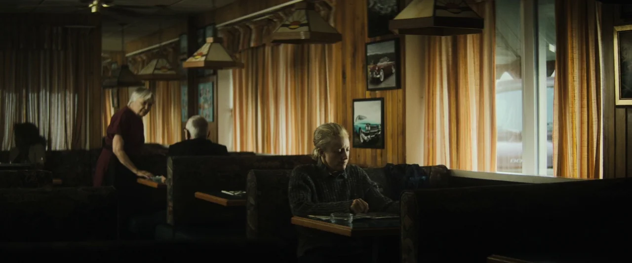 The Grudge (2020) movie still: medium — A diner booth features wood-paneled walls and vintage-style lamps with retro artwork framed nearby. A woman…
